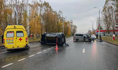Машина скорой помощи и перевёрнутый автомобиль на мокрой дороге, вдали другие машины и люди, оградительный конус. Тюмень, осень.