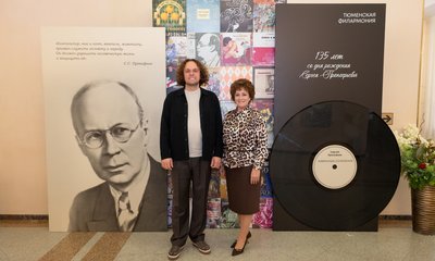 Мужчина и женщина у стенда Тюменской филармонии к 135-летию со дня рождения Сергея Прокофьева с его портретом и виниловой пластинкой.
