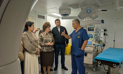 Врач в синей форме беседует с посетителями в операционной с хирургическим столом, лампами и аппаратурой.