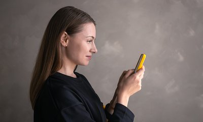 Женщина в чёрном смотрит в жёлтый телефон.