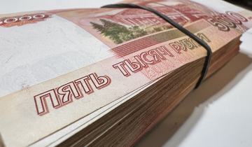 Крупный план толстой пачки банкнот номиналом 5000 рублей, перетянутой чёрной резинкой.