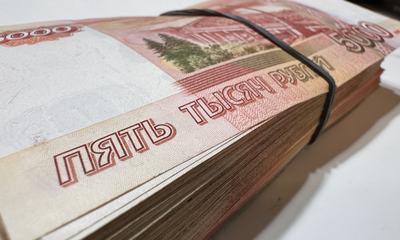 Крупный план толстой пачки банкнот номиналом 5000 рублей, перетянутой чёрной резинкой.