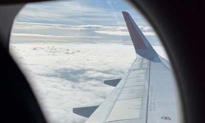 Крыло самолёта над облаками в окне иллюминатора.
