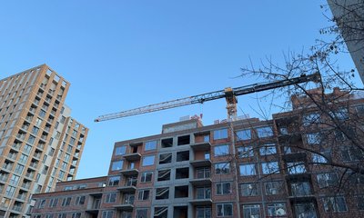 Новостройка с краном и готовая высотка на фоне голубого неба.